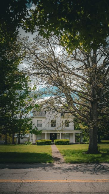 Classic white house surrounded by trees under a bright, cloudy sky in Ohio.