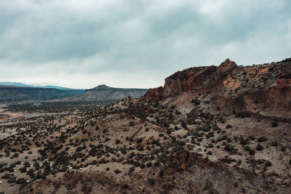 Aerial view of dramatic desert cliffs and shrubs in White Rock, New Mexico under a cloudy sky.