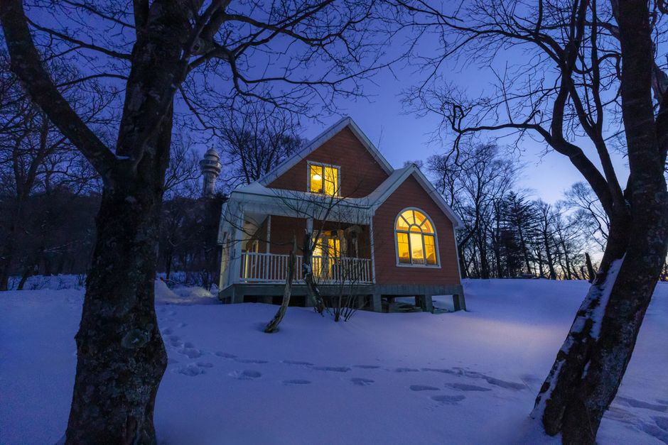 Snowy cabin glowing at twilight among winter trees