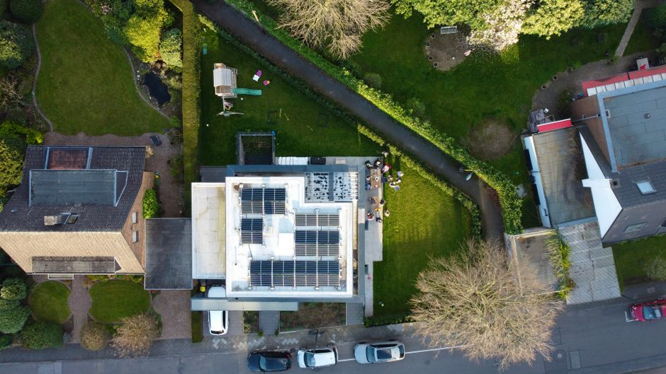 Aerial view of suburban houses featuring solar panels on rooftops and green gardens.