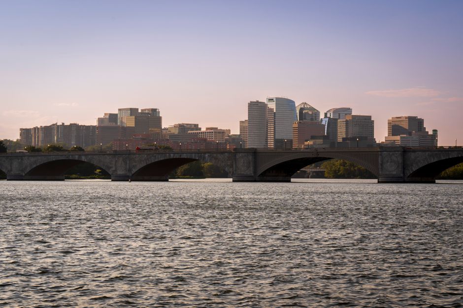 View of Arlington Memorial Bridge with modern skyline and calm river under twilight sky.