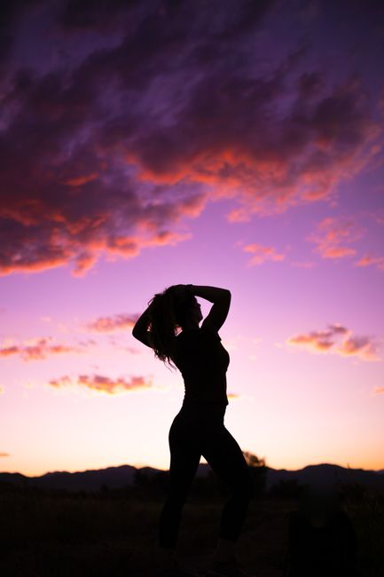 Dramatic silhouette of a woman posing against a vibrant sunset sky in Arvada, Colorado.