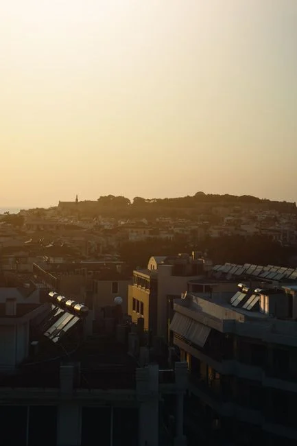 Silhouetted cityscape and rooftops under a warm sunset sky, capturing a peaceful urban scene.