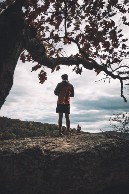 A man wearing a hoodie stands on a cliff, gazing at the scenic landscape in Arkansas.