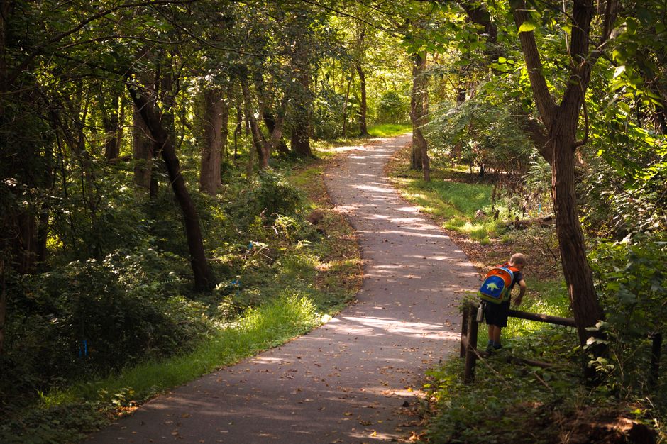 A kid with a colorful backpack explores a wooded trail in Bethesda, Maryland.