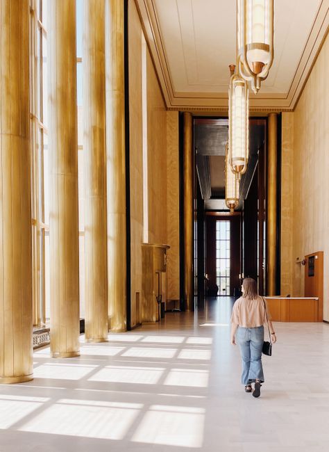 Interior view of a grand hall in Bismarck with a lone woman walking, casting shadows from large windows.