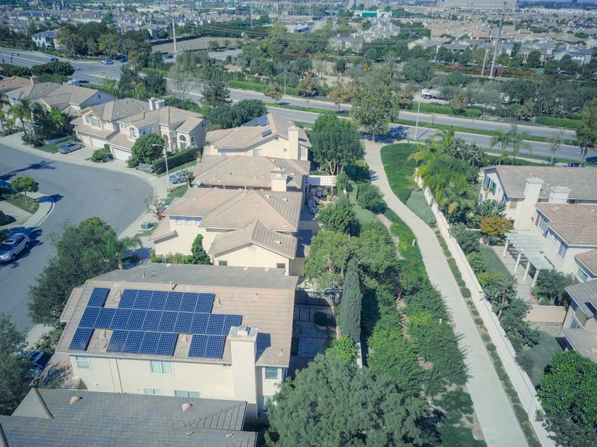 Aerial shot of suburban homes featuring solar panels and green landscapes.