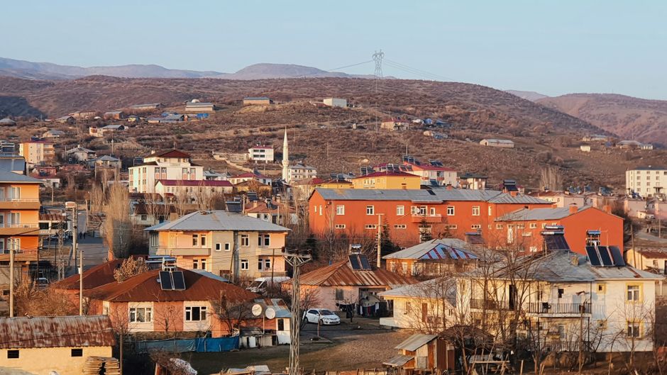 Aerial view of a small town nestled in hills with colorful residential buildings under a clear sky.