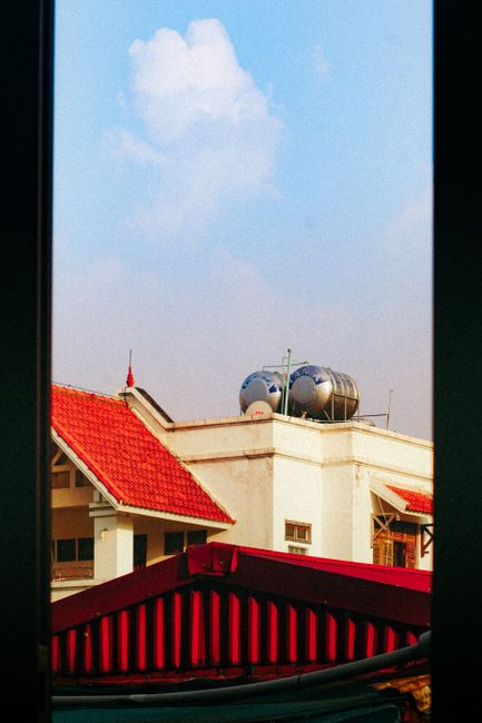 View of red-roofed buildings and tanks under a clear blue sky seen through a window frame.