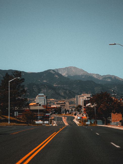 A city road leading to mountains in Colorado Springs under a clear sky.