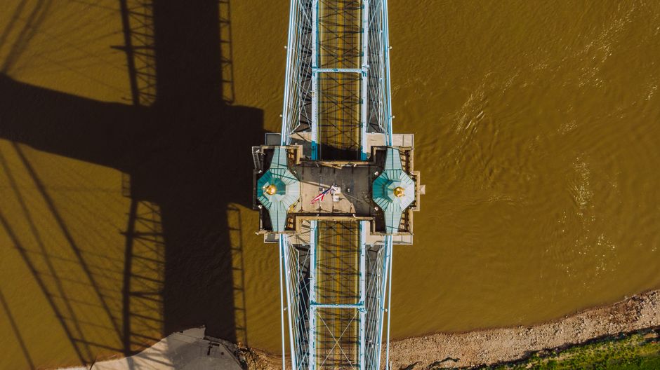 Drone view of blue metallic Cincinnati Covington Bridge over Ohio River casting shadow onto water surface in Kentucky in USA