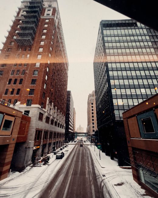 A snowy urban street in Des Moines, Iowa, flanked by tall buildings, captured during daylight.