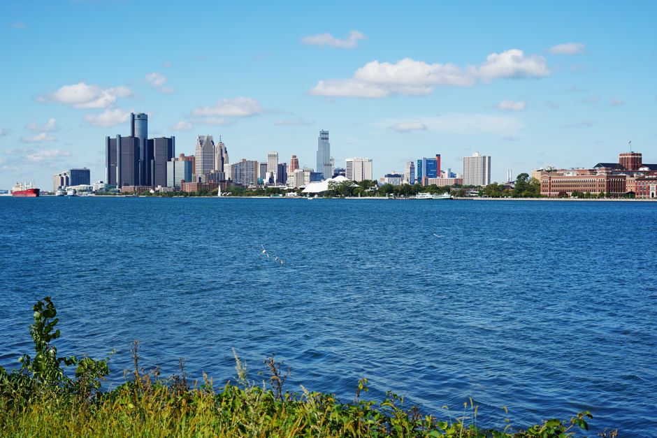 Panoramic view of Detroit skyline across the river, showcasing iconic buildings on a sunny summer day.