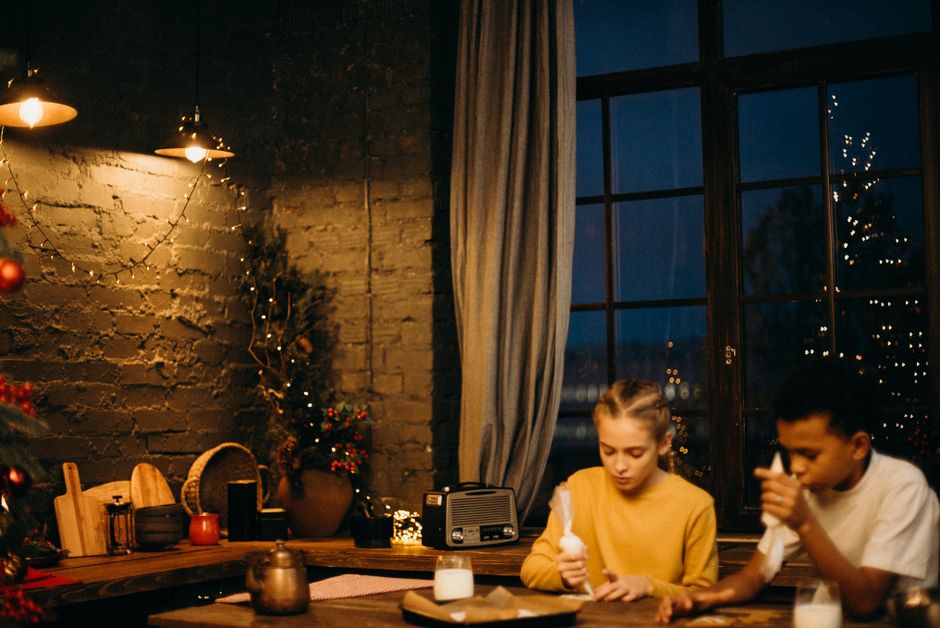 Two children decorating gingerbread cookies indoors by candlelight, creating a cozy holiday atmosphere.