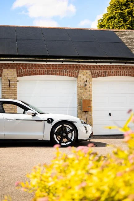 A white electric car charges at a home station with solar panels.