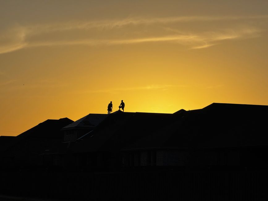 Two workers silhouetted on a roof during a golden Fort Worth sunset, Texas, USA.