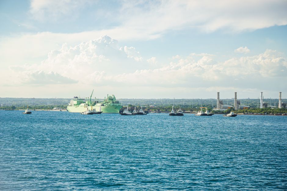Vibrant blue sea with docked ships and industrial structures under a partly cloudy sky.