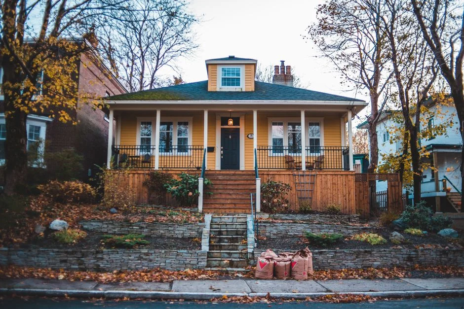 Cozy yellow bungalow surrounded by autumn leaves in a quiet suburban neighborhood.