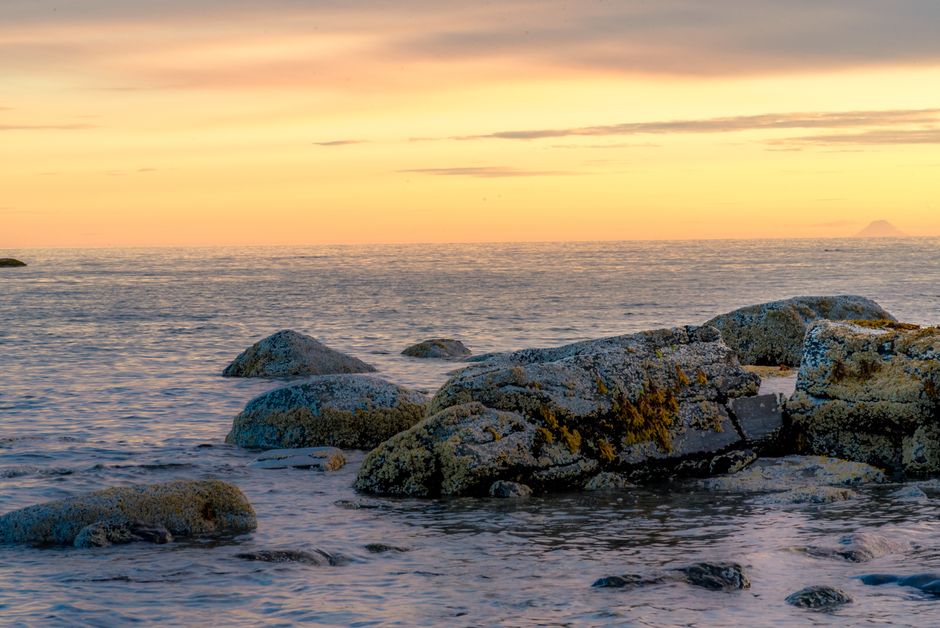 Calm sea view with rocks at sunset in Homer, Alaska, reflecting serene coastal beauty.