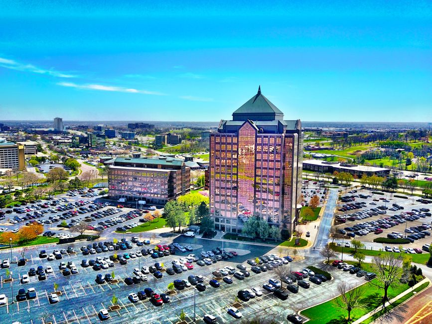 Bird's-eye view of a modern skyscraper and parking lot in Overland Park, KS, under a clear blue sky.