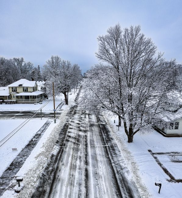 Snow-covered suburban street captured from above during winter.