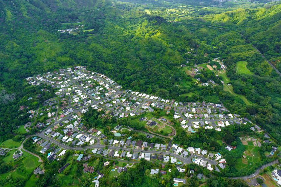 Aerial view showcasing a lush green valley with suburban town, hills, and forests.