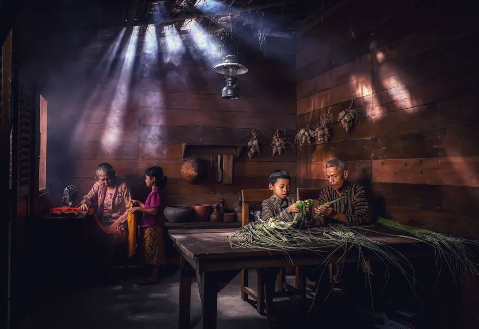 A family in Jakarta crafting in a sunlit wooden room with traditional items.