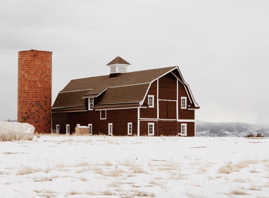 A charming red barn and silo stand amid a snowy winter landscape in Littleton, Colorado.