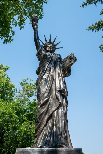 Bronze replica of Statue of Liberty in Longmont, Colorado, surrounded by trees.