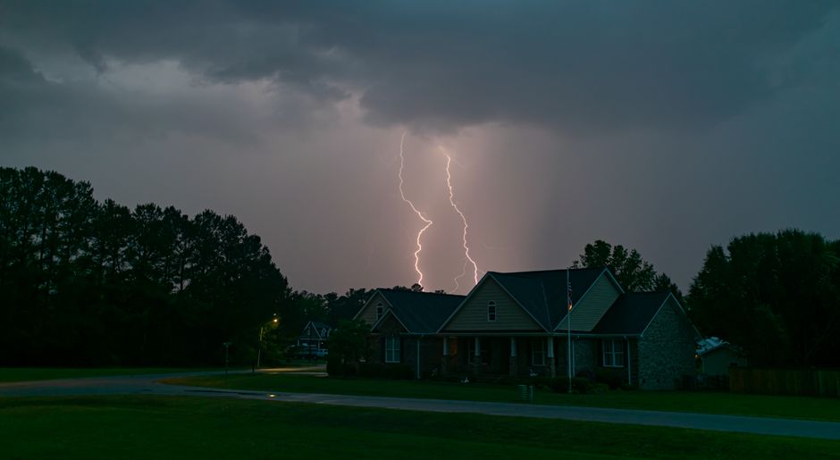 A powerful lightning bolt illuminates a suburban neighborhood under an overcast sky.
