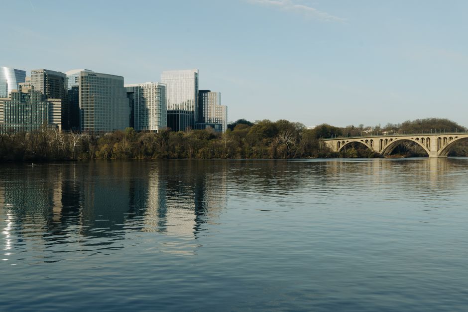 A scenic view of skyline buildings and Key Bridge reflecting on the Potomac River.