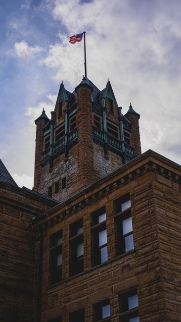 Low-angle shot of a historic courthouse tower featuring an American flag against a cloudy sky.