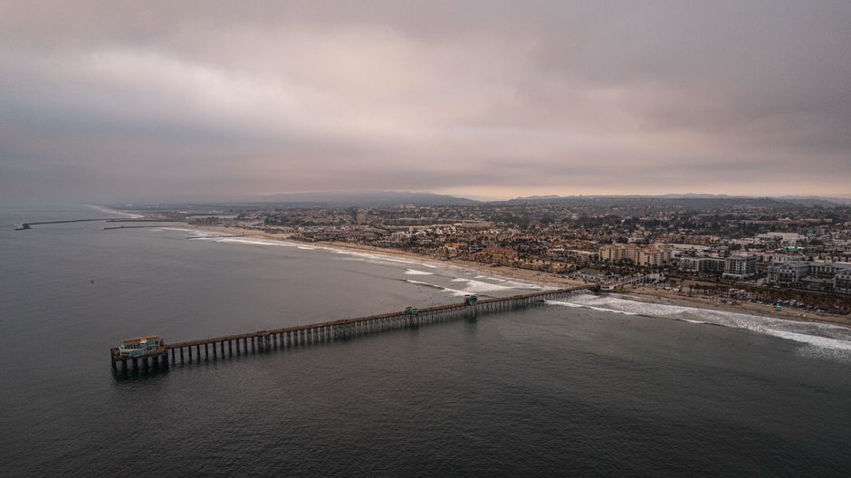 Drone shot of Oceanside Pier and coastline in California under a cloudy sky in the evening.