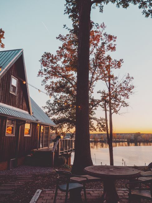 Cozy cabin by the lake with warm lights under a vibrant sunset sky.