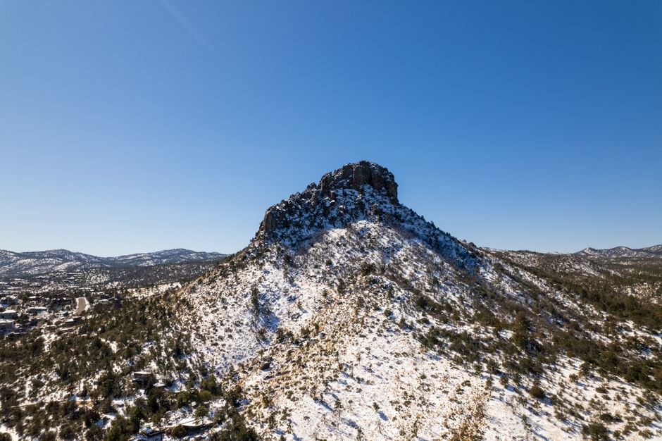 Aerial view of Thumb Butte mountain covered in snow against a clear blue sky in Prescott, Arizona.