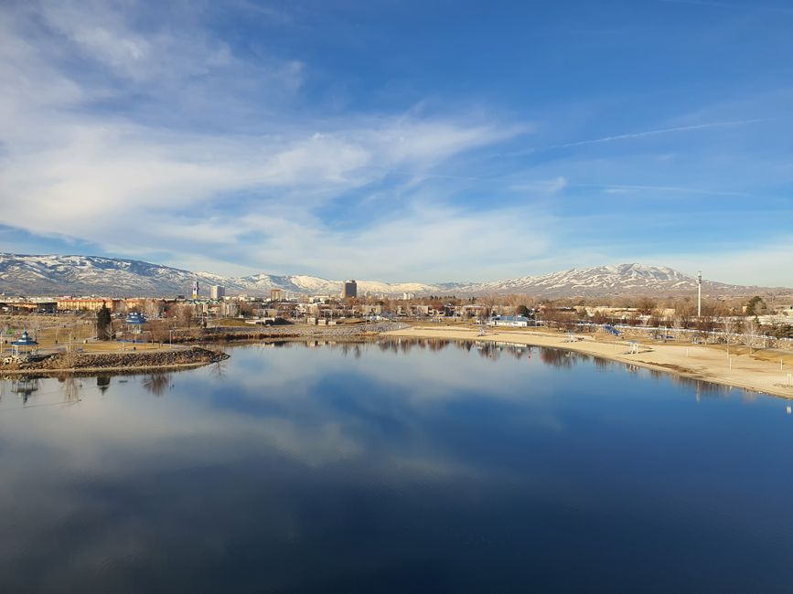 Discover Reno's skyline reflecting on a tranquil lake with snow-capped Sierra Nevada mountains in the background.