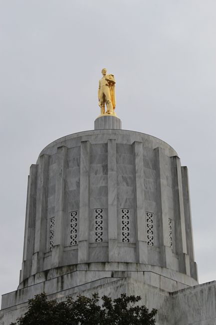 Vertical shot of the Oregon State Capitol with a prominent golden statue on top against a cloudy sky.