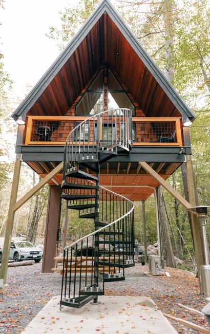 Stunning elevated wooden cabin with a spiral staircase set in a lush forest setting, Sanford Maine.