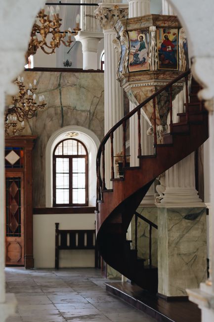 Intricate spiral staircase within a historic chapel interior featuring religious artwork.