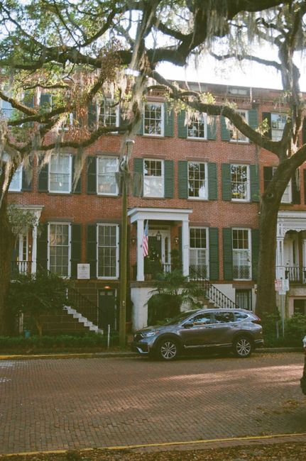 Elegant brick townhouse with green shutters on a historic street in Savannah, Georgia.
