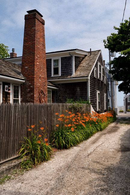 Historic New England house in Provincetown with vibrant summer flowers and chimney.