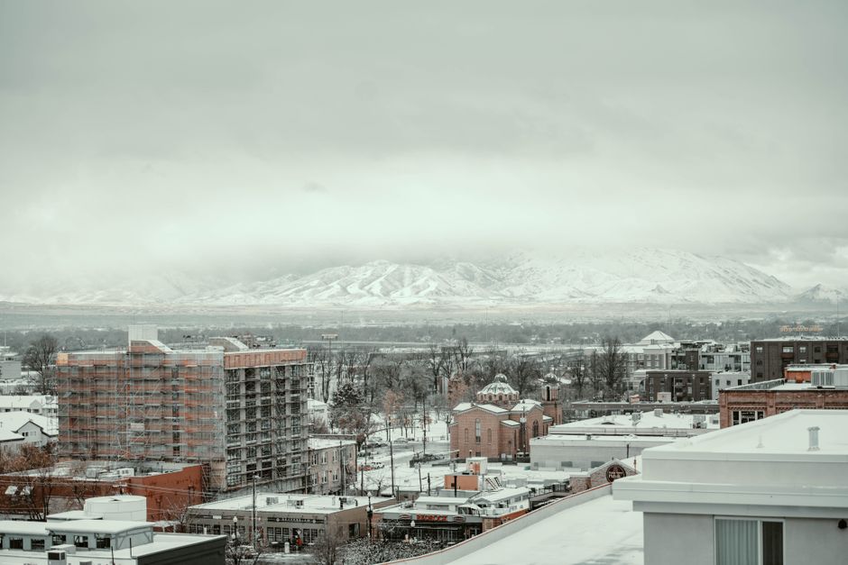 A winter cityscape view in Salt Lake City with snow-covered buildings and mountains in the background.