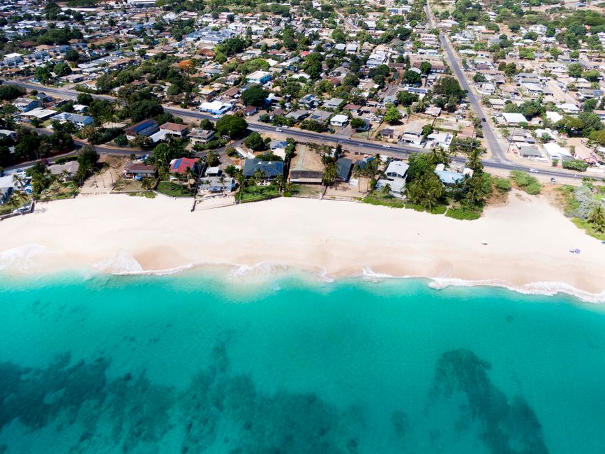 Aerial shot of Waianae, Hawaii's beachfront showcasing turquoise waters, sandy beach, and residential area.