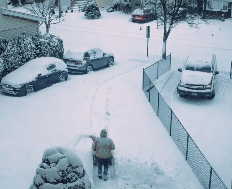 A person shoveling snow in a suburban driveway after a fresh snowfall, showcasing winter chores.