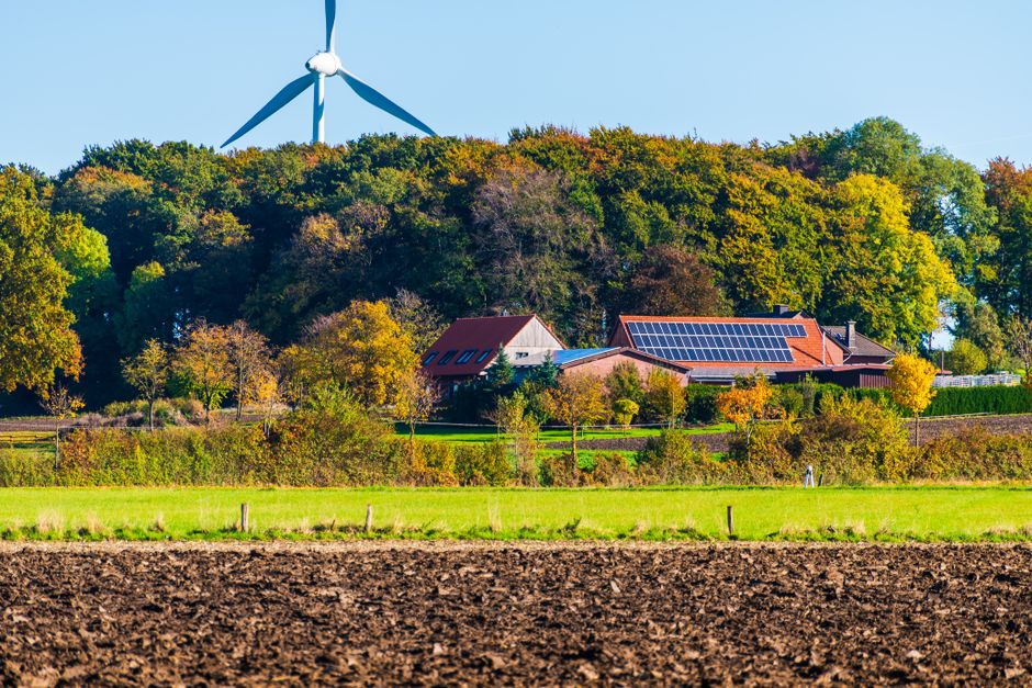 A picturesque sustainable farm featuring wind turbine and solar panels surrounded by vibrant autumn foliage.